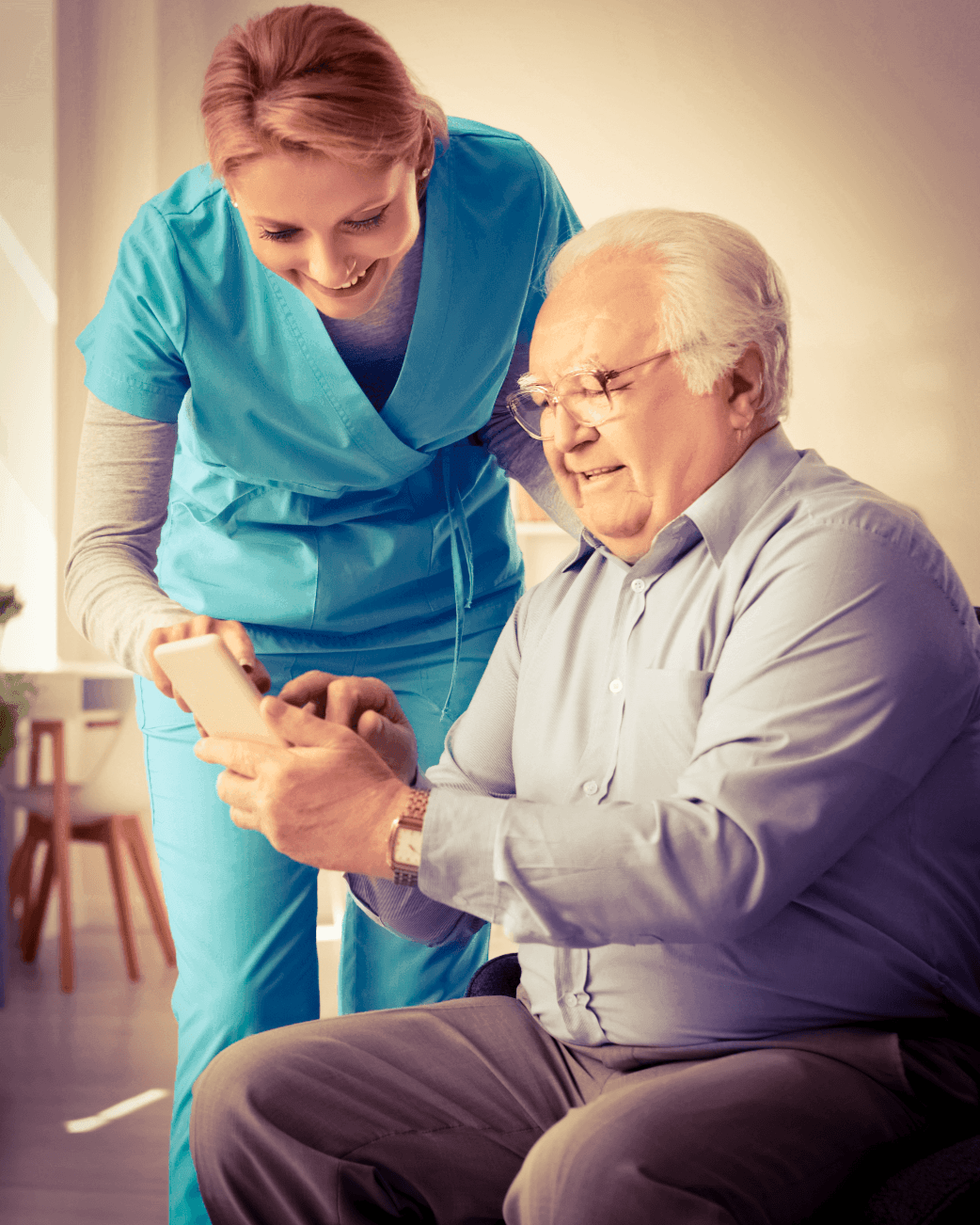 Caregiver assisting an older man with using a smartphone at home.