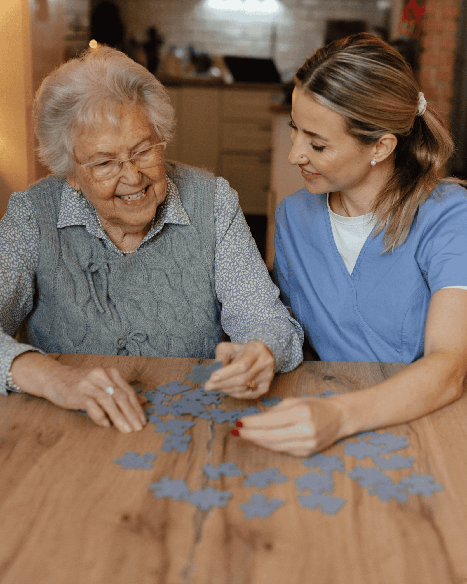Caregiver and senior woman smiling together while doing a puzzle at a table.